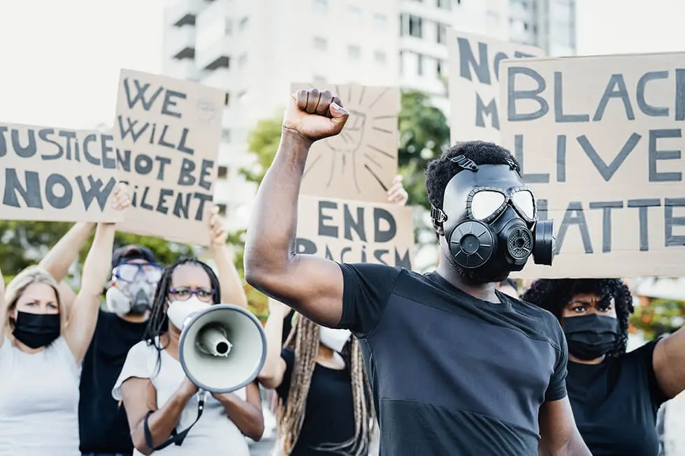 Protesters with signs advocating for justice and ending racism, some wearing masks