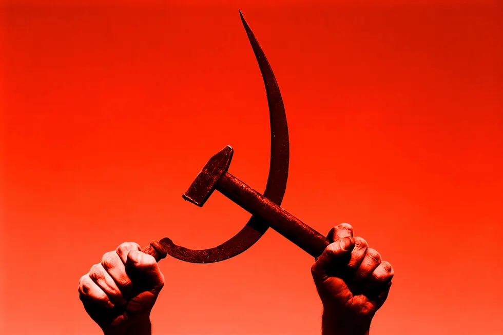 Hands raised holding a hammer and sickle against a red background, a symbol of communism